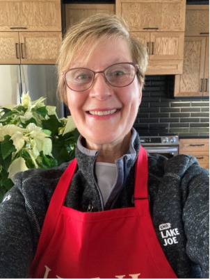 Monique is in her kitchen wearing a red apron with a big smile.