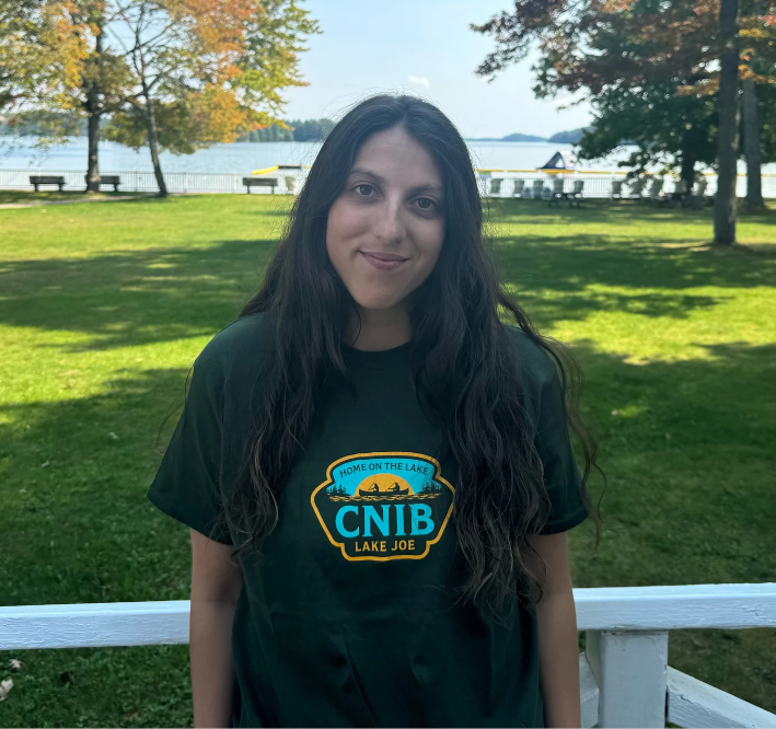 Stela se tient sur la promenade du camp Lake Joe d'INCA et elle tourne le dos au lac. Elle porte un t-shirt vert olive du camp Lake Joe d'INCA.