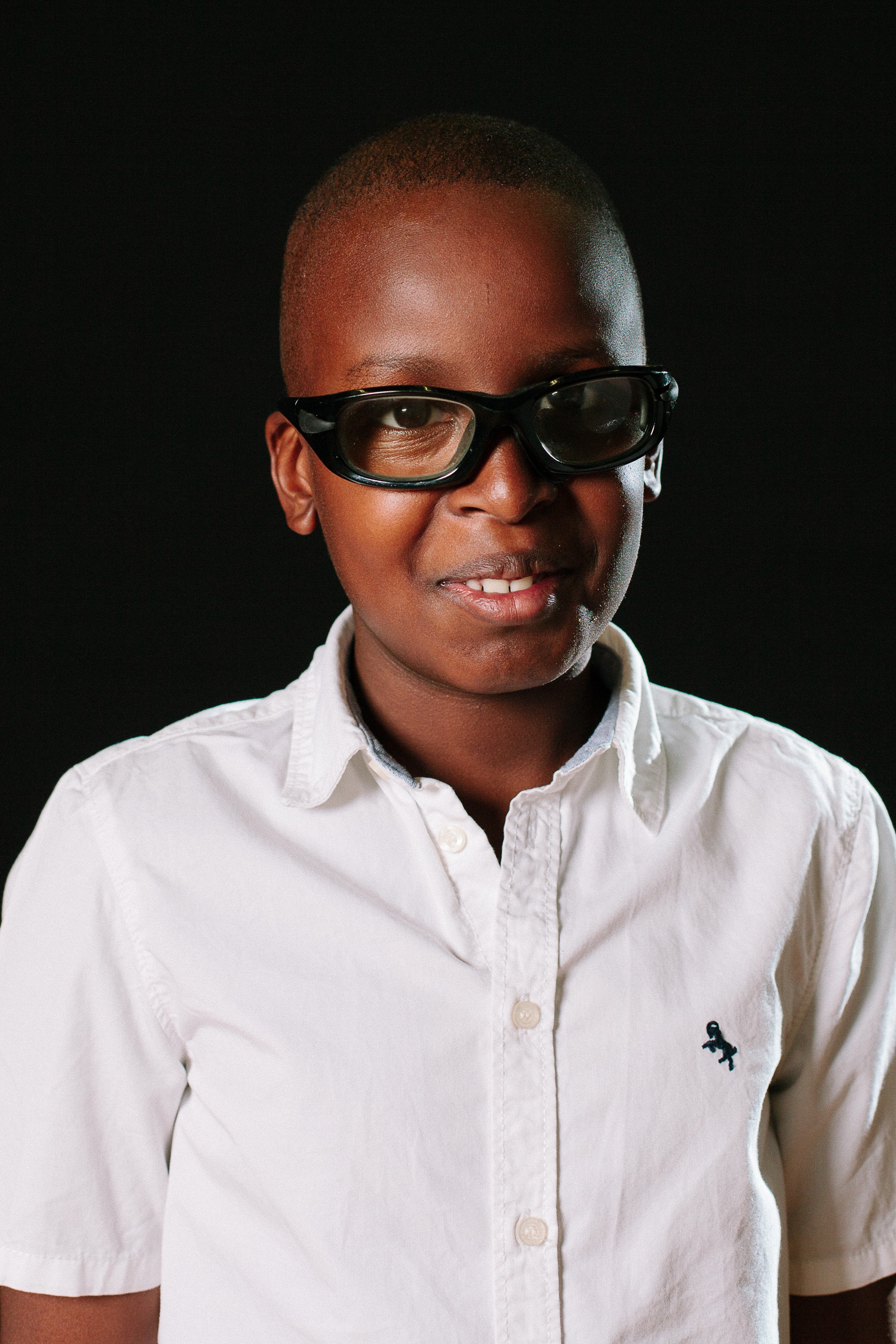  A school photo of a smiling Steve. He is wearing blue glasses and a white shirt.