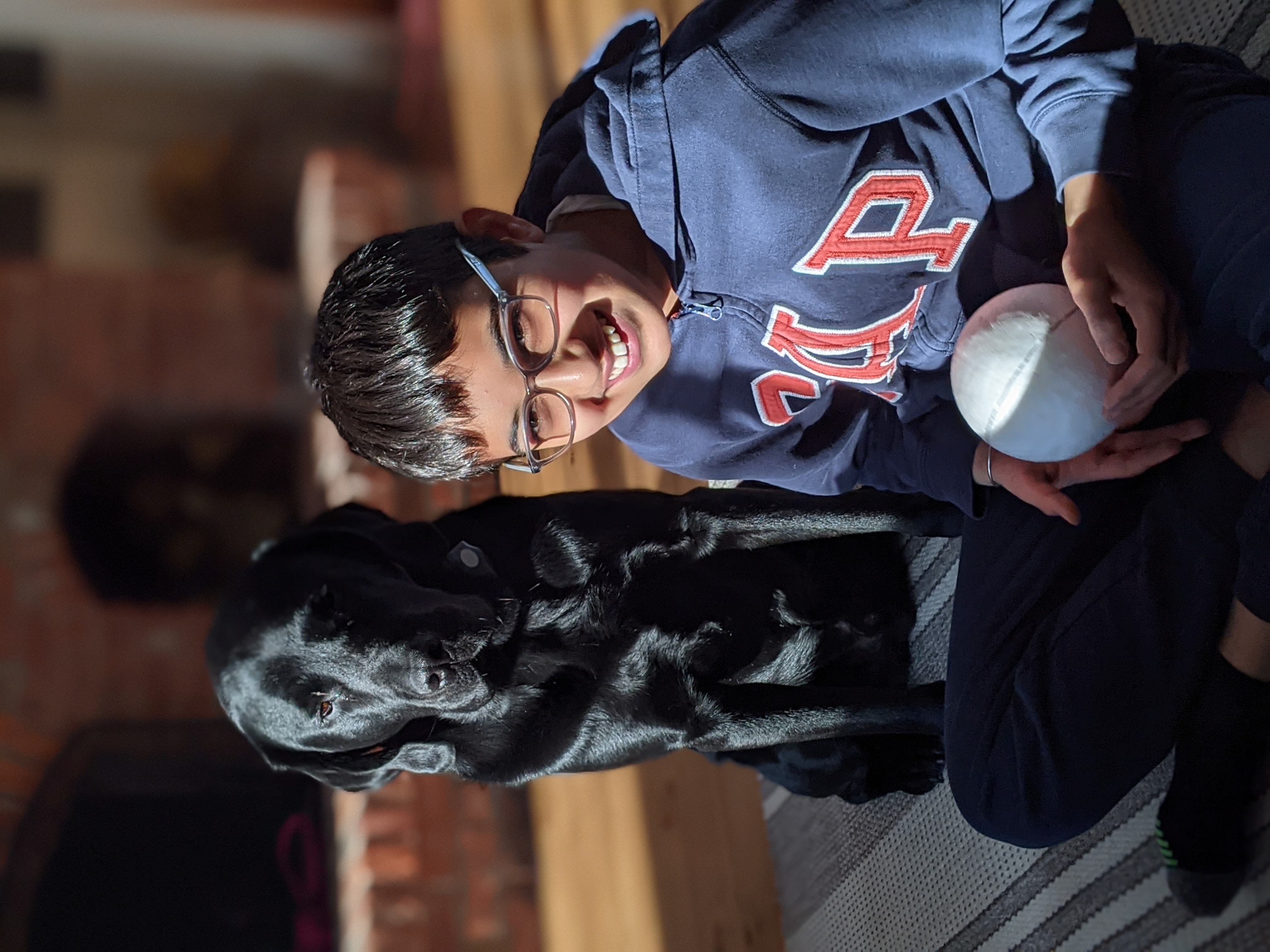 Surya sitting cross-legged on the floor smiling, with Isaiah sitting next to him in the sun.