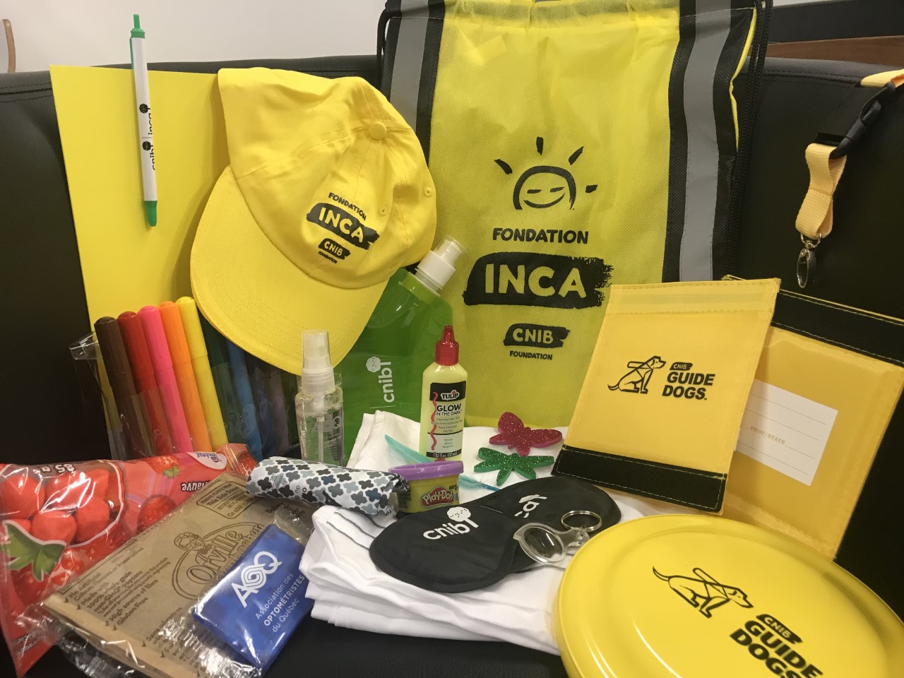 Articles de la trousse « Camp emballée ». Un sac et une casquette à l'effigie de la Fondation INCA, ainsi qu'un frisbee du programme de chiens-guides, des articles de bricolage et des collations, le tout remis aux jeunes participants aux camps. 