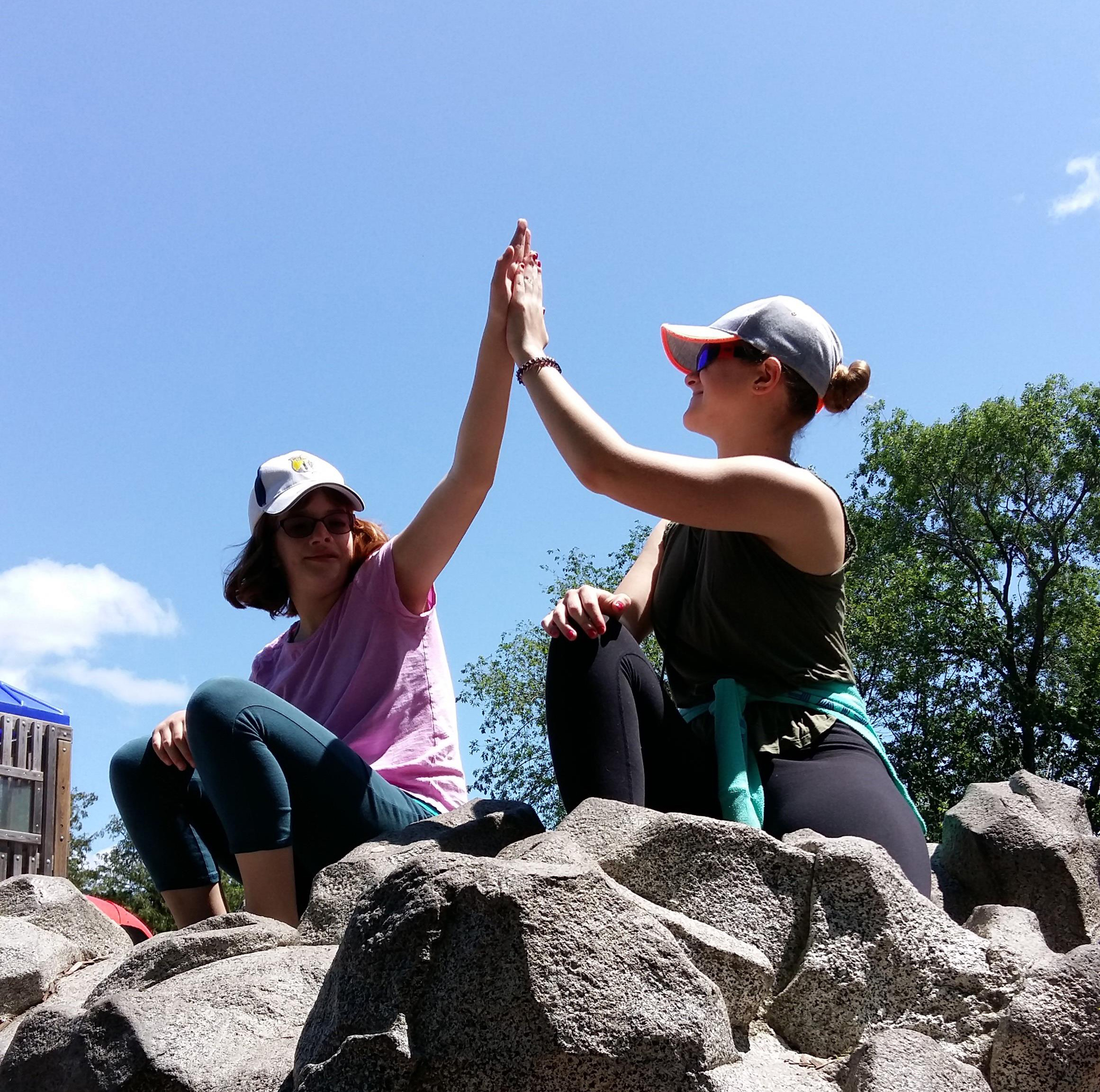 Emilee and Hannah sitting on top of a mountain and high-fiving.