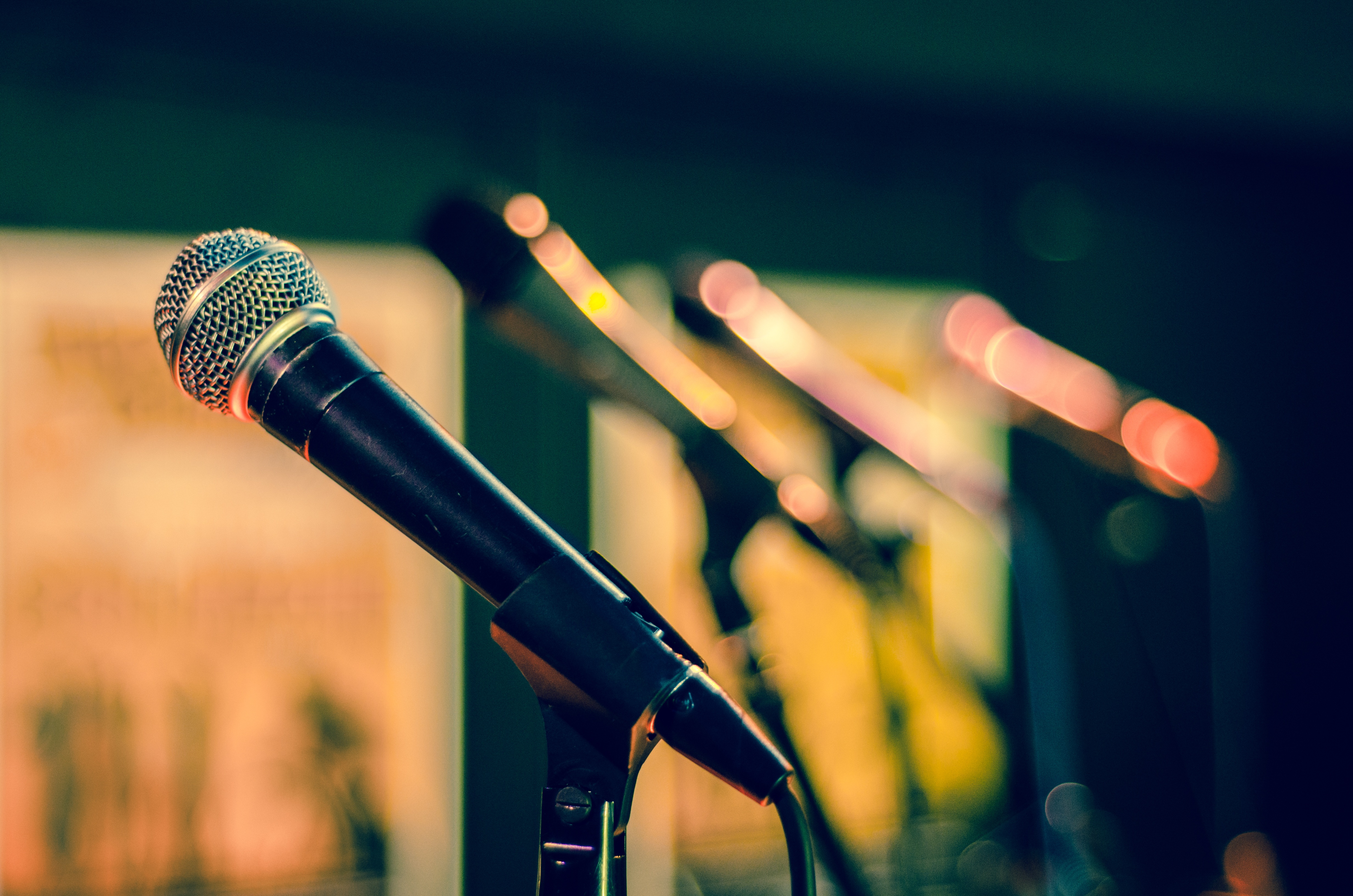 Image shows a line of microphones in their stands on a stage.