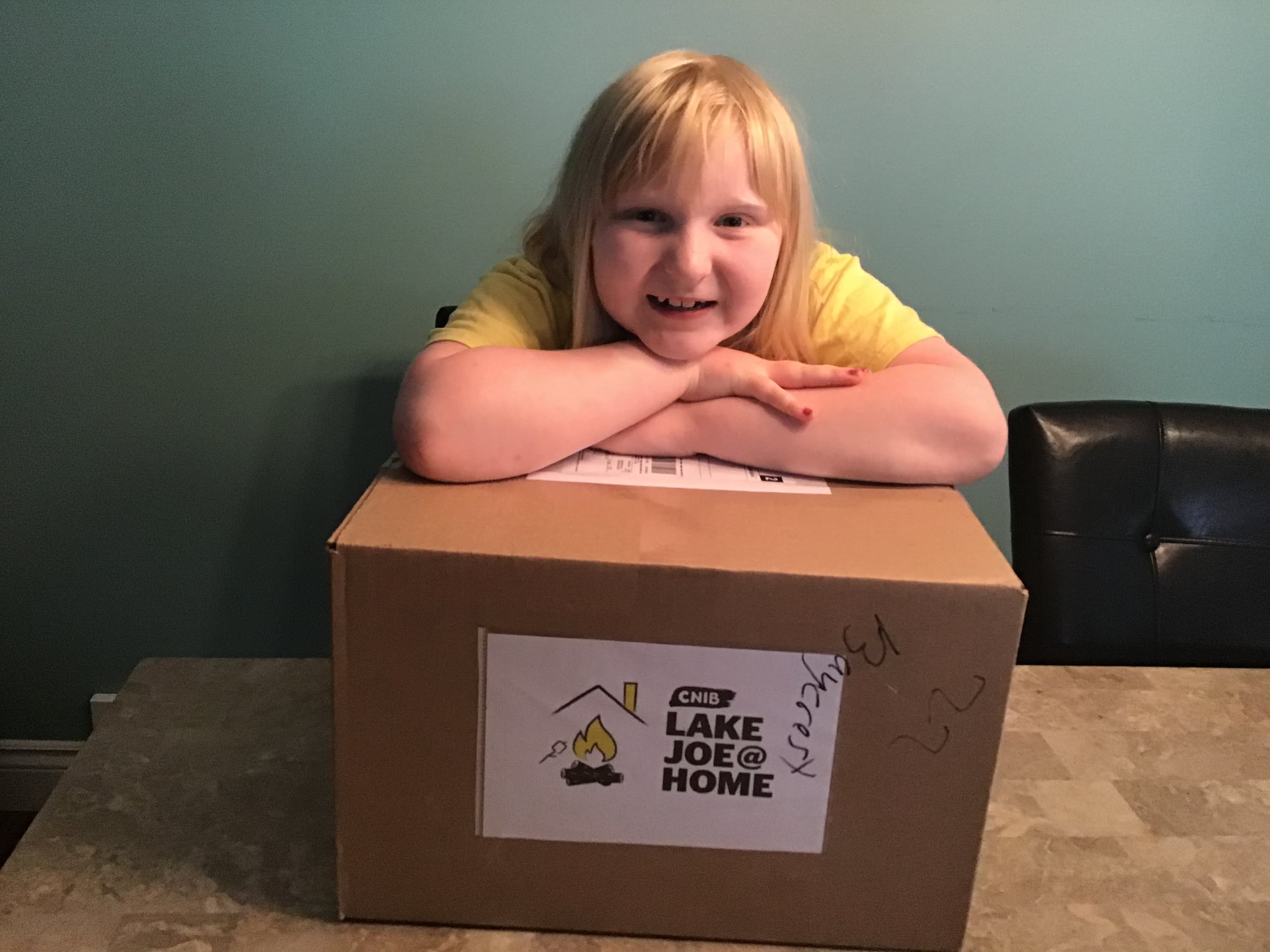 CaA young girl poses for a photo leaning on top of her camp-in-a-box, a cardboard box.