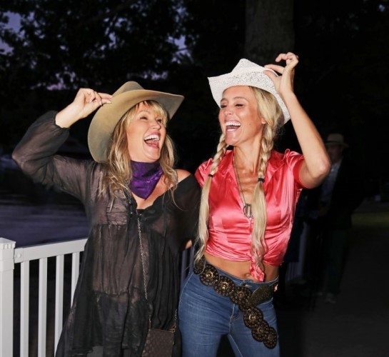 Deux invitées souriantes se tiennent par le bras et touchent leur chapeau de cowboy.