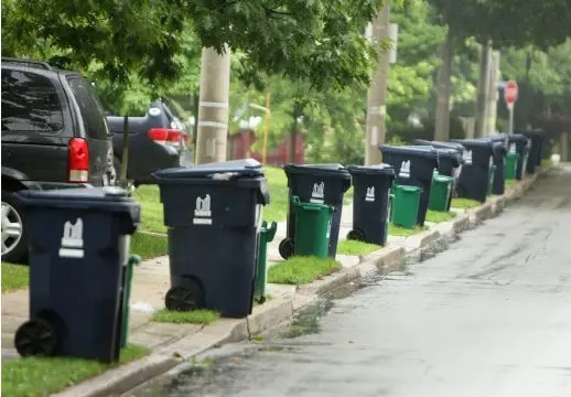 Bacs de poubelles et sac de recyclage bien cordé dans l'espace réservé sur le trottoirs, en dehors de la voie piétonne.