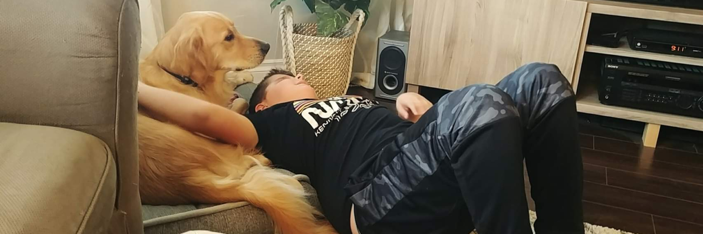 Landon et son chien-compagnon d'INCA Ruggles, un Golden Retriever, allongés ensemble sur un coussin dans leur salon. Le bras de Landon est étendu pour pourvoir flatter le dos de Landon.