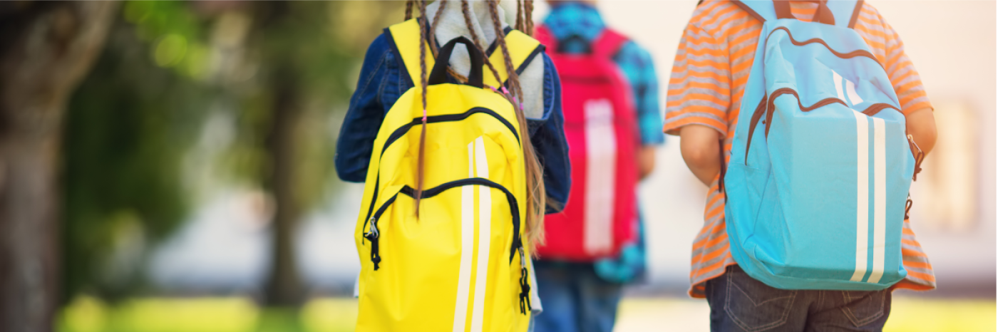 Trois jeunes de dos se rendant à l'école. Ils portent des sacs à dos et sont à l'extérieur.