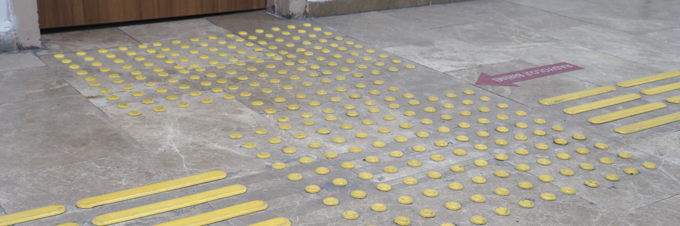 Un sol carrelé avec un pavage tactile/des indicateurs tactiles de surface d'orientation Le pavage est constitué de points et de lignes jaunes en relief. 
