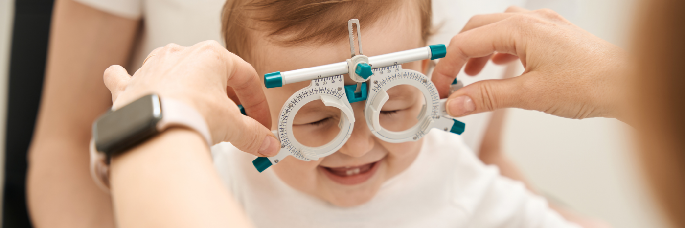 Un optométriste procède à un examen de la vue sur un jeune enfant. Il tient d'une main un cadre d'essai optométrique devant le visage de l'enfant.
