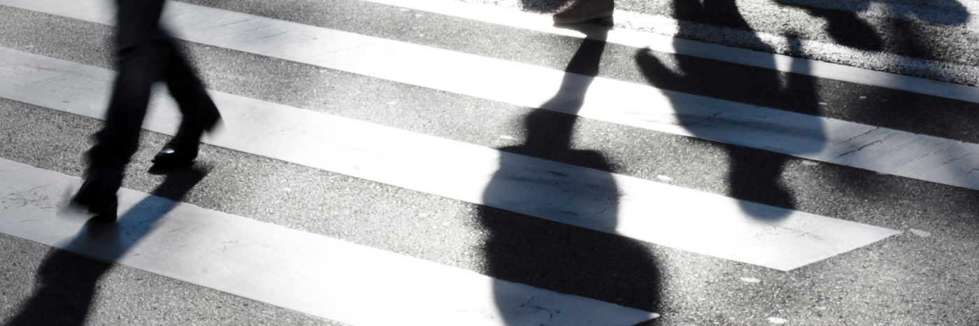 Un passage piéton avec les ombres de personnes qui marchent. L'image est en noir et blanc et montre les jambes de plusieurs personnes qui traversent une rue. 