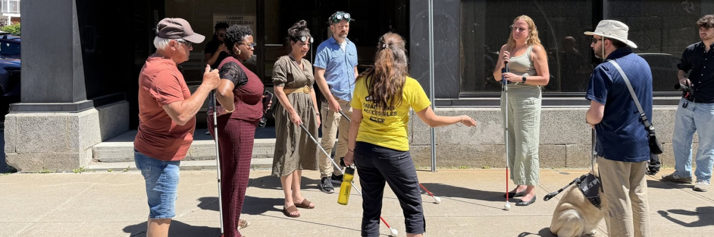  Sarah Rouleau donne des instructions pour le défi à l’aveugle aux participants de la campagne Montez à bord! Sont présents Thama Cherilus, David Demers, le directeur d’INCA Québec, Annie Provencher, conseillère du district Carmel, Pierre Luc Fortin Conseiller municipal, district des Estacades, Ville de Trois-Rivières ainsi que Karine Descoteaux, directrice générale de l’ARÉA. Plusieurs participants tiennent une canne blanche et le chien-guide de David Demers est assis près du groupe pendant les échanges.