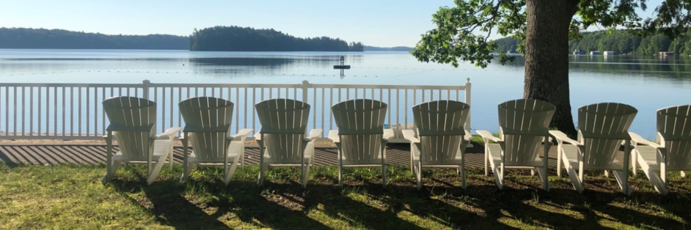 Une rangée de chaises blanches Muskoka est assise sur la rive du lac Joe.
