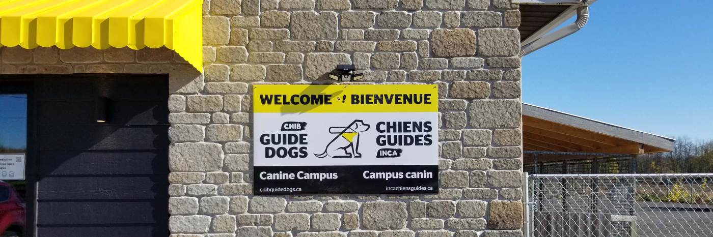 Une photo du panneau de bienvenue placé à l'extérieur du Campus canin. On peut y lire : « Welcome et Bienvenue » avec le logo des chiens-guides d'INCA au milieu du panneau