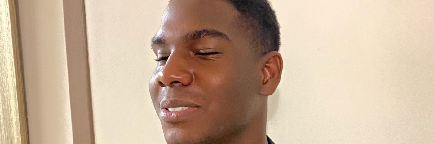 Photo de Michel-Antony, un jeune homme noir au cheveux courts portant un chandail jaune et un veston gris foncé.