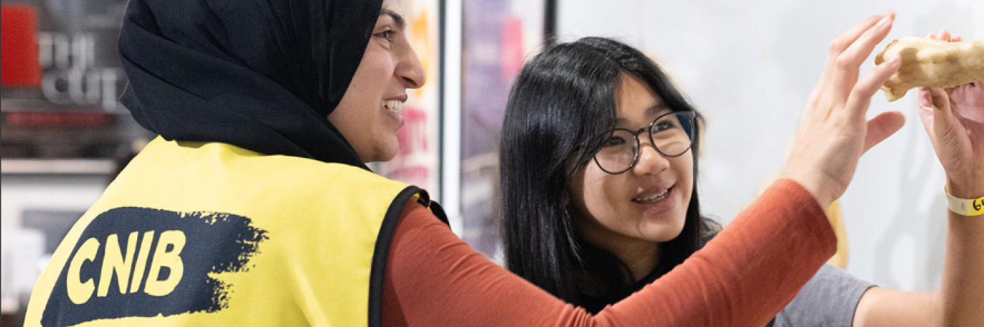 Deux femmes, dont l'une porte un gilet d'INCA, sourient tout en tenant et en examinant ensemble un objet à l'intérieur.
