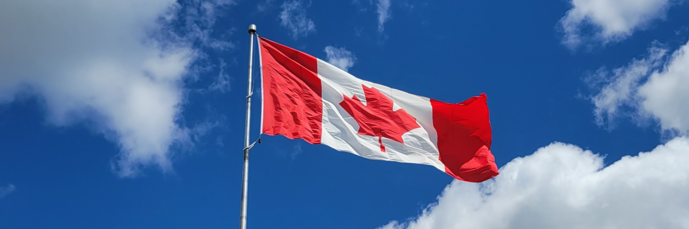 Un drapeau canadien flotte au sommet d'un mât, sur fond de ciel d'un bleu éclatant.