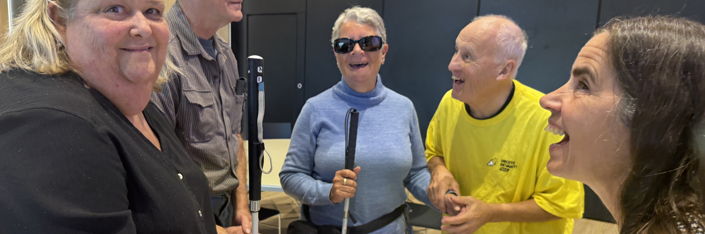 Un homme portant un chandail jaune discute et sourie avec des personnes aveugles.
