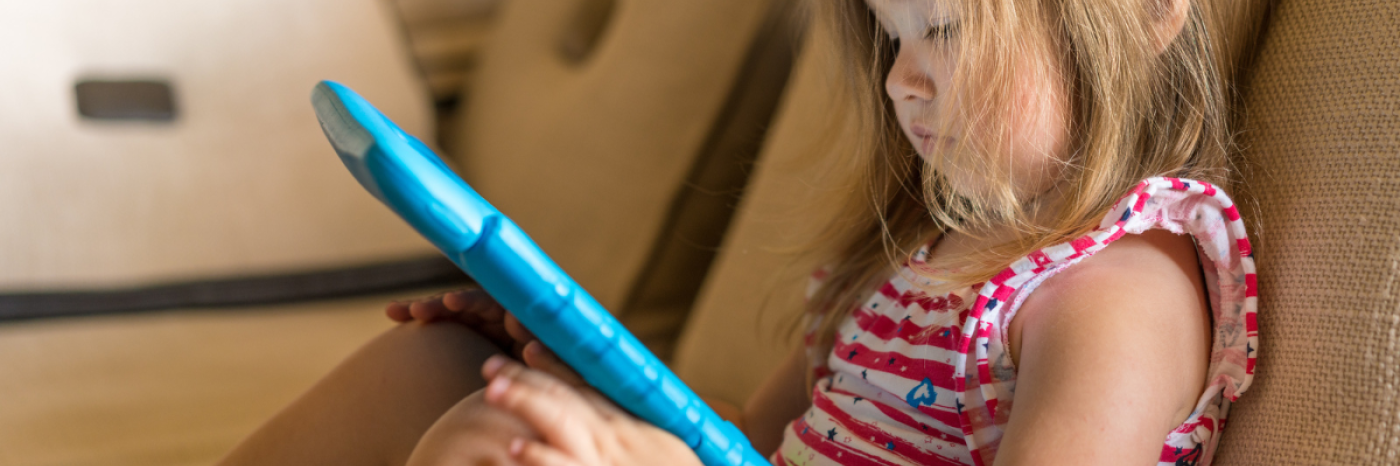 Une jeune fille est assise sur un canapé et joue sur une tablette. La tablette est protégée par un étui en caoutchouc bleu.