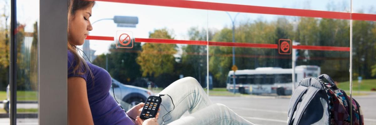 Photo of young woman relaxing, reading an audiobook, waiting at bus stop.