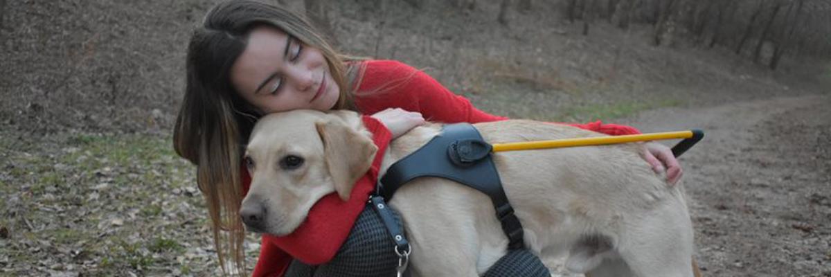 Danika étreignant un labrador croisé golden retriever avec un harnais jaune.