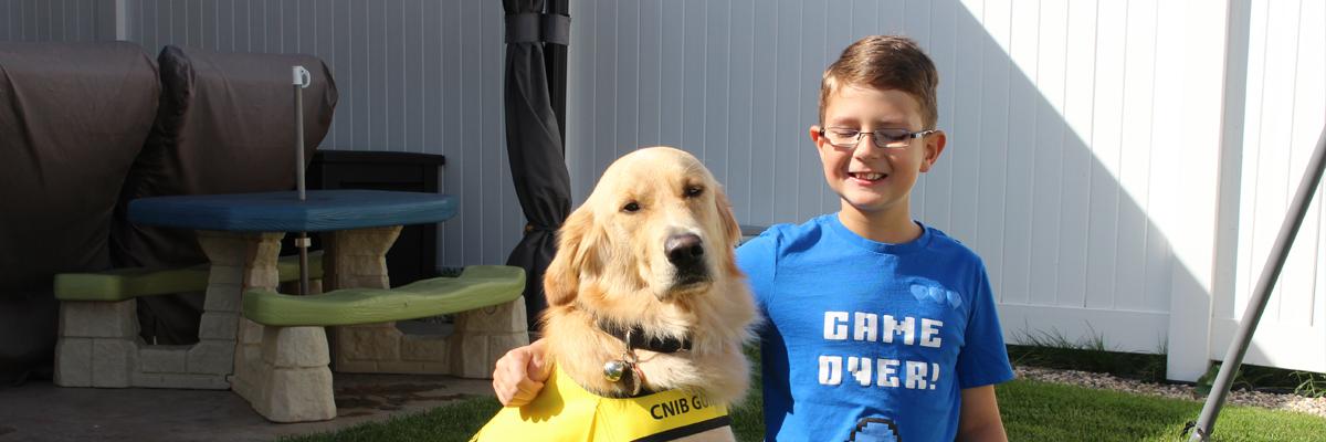 Un garçon souriant portant des lunettes avec son bras autour d'un Golden Retriever qui porte une veste jaune.