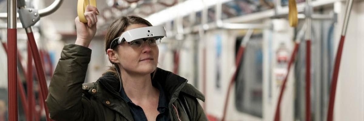 A woman wearing eSight glasses stands in a subway car.