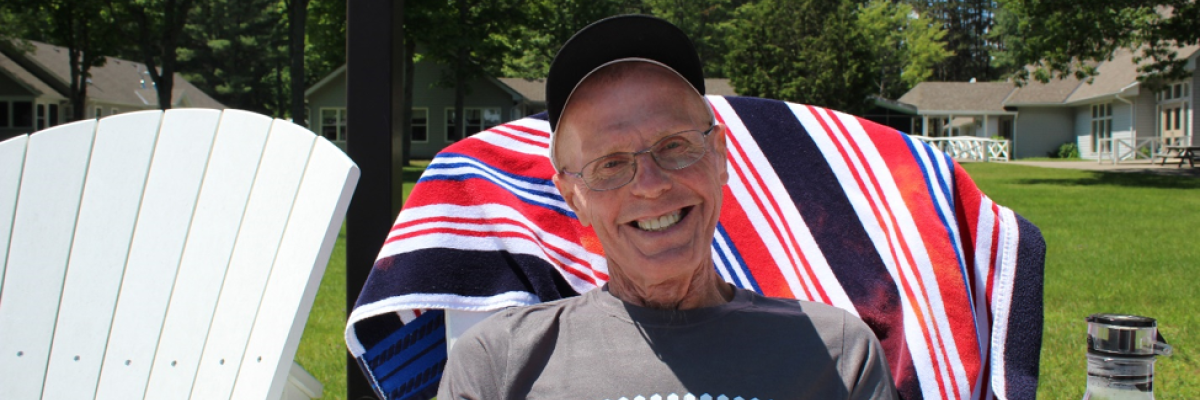 Jim (and his megawatt smile) sits in a Muskoka chair near the shores of CNIB Lake Joe.  