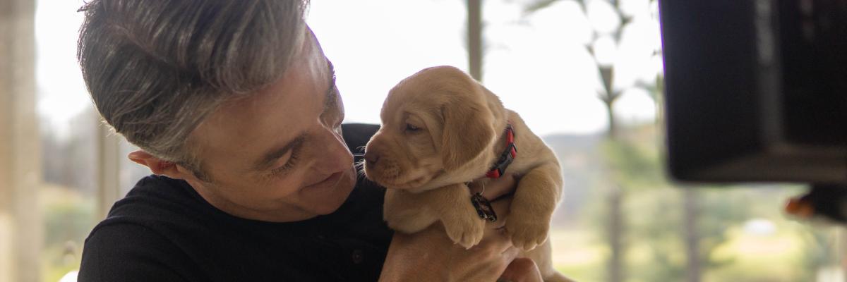 Ben Mulroney tenant un chiot d'à peine quelques semaines, un Labrador-Retriever jaune.