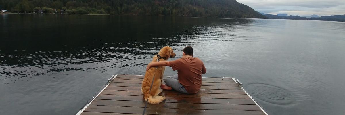 Landon et Ruggles, un Golden Retriever, assis sur un quai surplombant un lac; Landon passe son bras sur le dos de Ruggles qui regarde son jeune maître