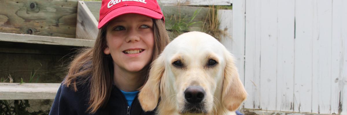 Zach and his CNIB Buddy Dog Elsie sitting in their backyard. Elsie is wearing her yellow CNIB Buddy Dog vest and Zach has his arm around her.