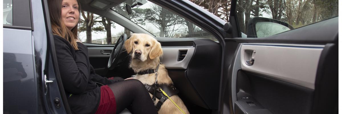 Une femme assise sur le siège du passager avant d'un taxi avec son chien-guide, un Golden Retriever, assis sur le sol à ses pieds, la portière grande ouverte