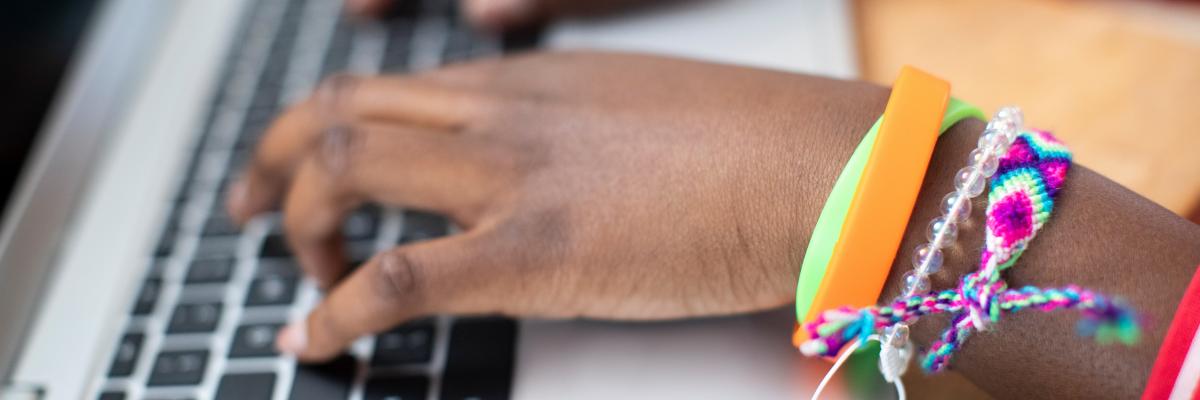 The hands of a teenager wearing friendship bracelets typing on a laptop computer.