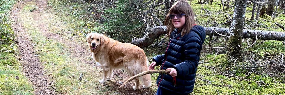 Rhea et son chien compagnon d'INCA, Ivy, un Golden Retriever de deux ans, marchent le long d'un sentier dans les bois. Rhea tient un bâton et tous deux regardent l'appareil photo en souriant.