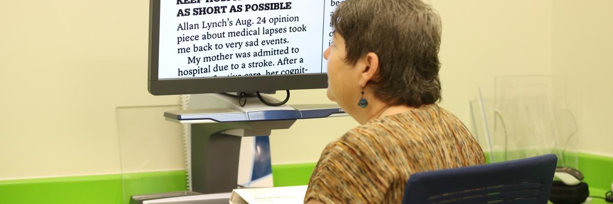 A woman sits at a CCTV and reads an enlarged document displayed on the screen.