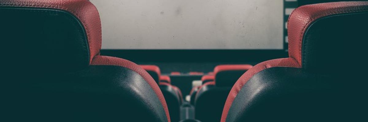 An empty movie theatre. Rows of chairs are stacked in front of dark movie screen.