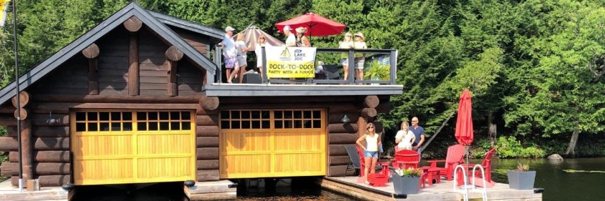 Picture from 2020 Dock-to-Dock event. People gathered on a boathouse and dock on a lake. 