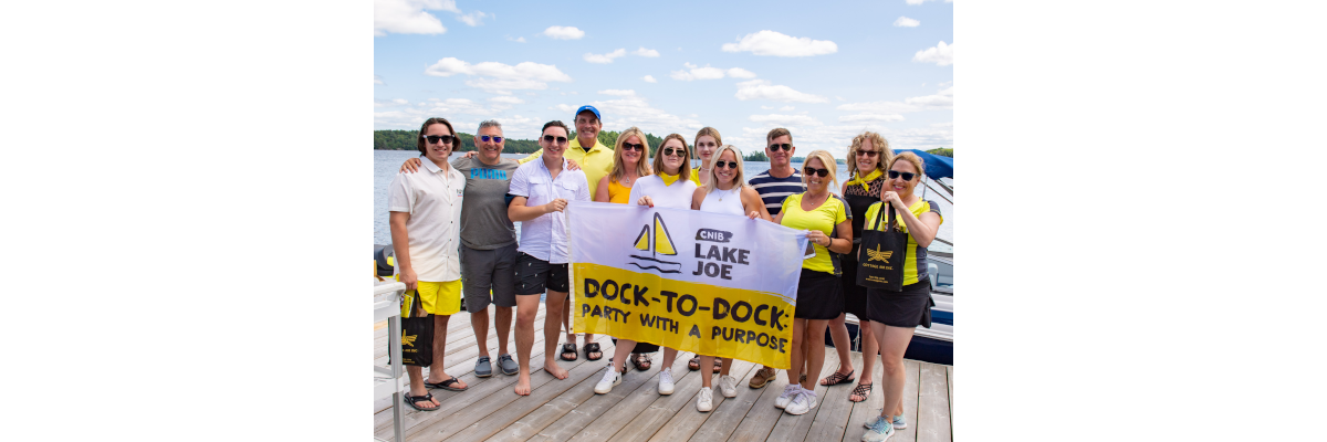 Des bénévoles de l’événement Muskoka de quai en quai d'INCA posent au hangar à bateaux du camp Lake Joe d’INCA, tenant des drapeaux à l’effigie de l’événement