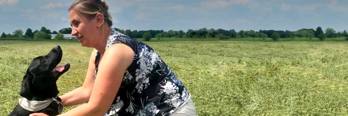 Louise kneeling on a sunny field, with her arms around Jess, who is sitting and smiling up at Louise. 