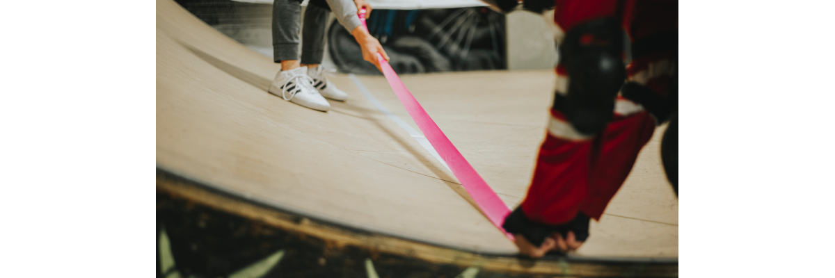 Two skateboarders place bright pink tape down on a skatepark ramp to create a more tactile/accessible skateboarding experience.