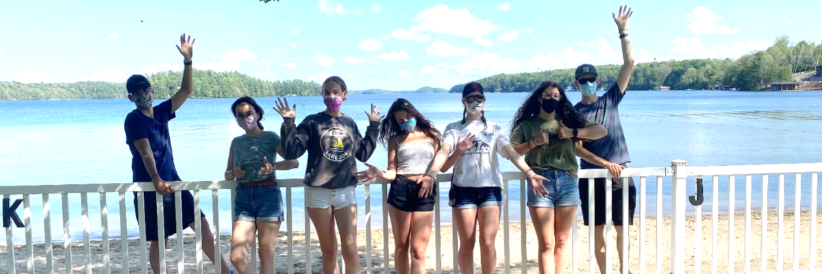 Seven 2021 seasonal staff members waving from the fencing on the waterfront.