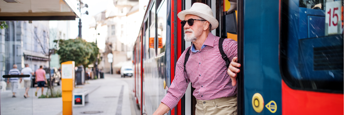 An older man using a white cane exits a city bus.