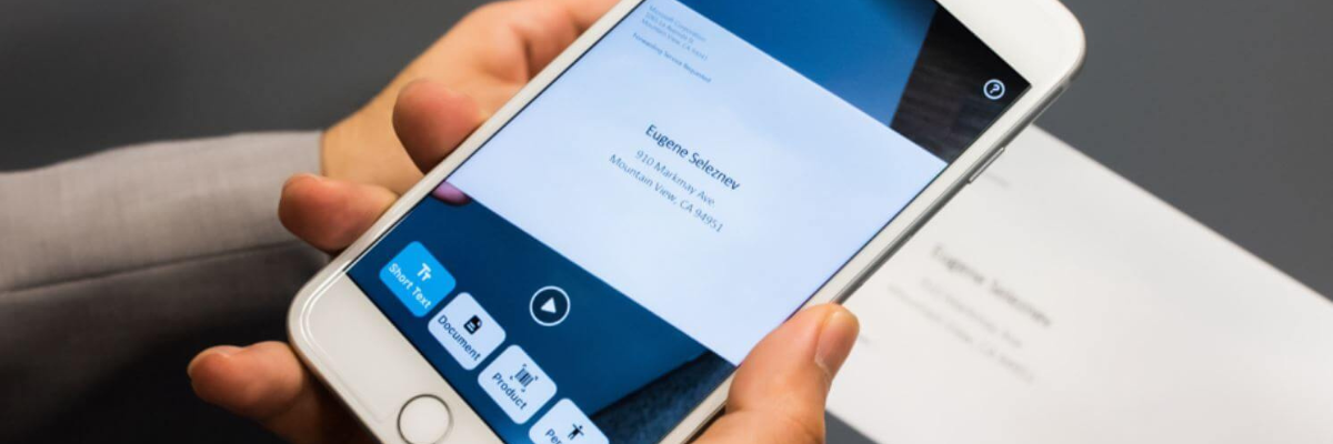 Two hands holding a smartphone up to a document. The phone camera is scanning the document and the seeing AI app is displayed on the phone screen. © Microsoft