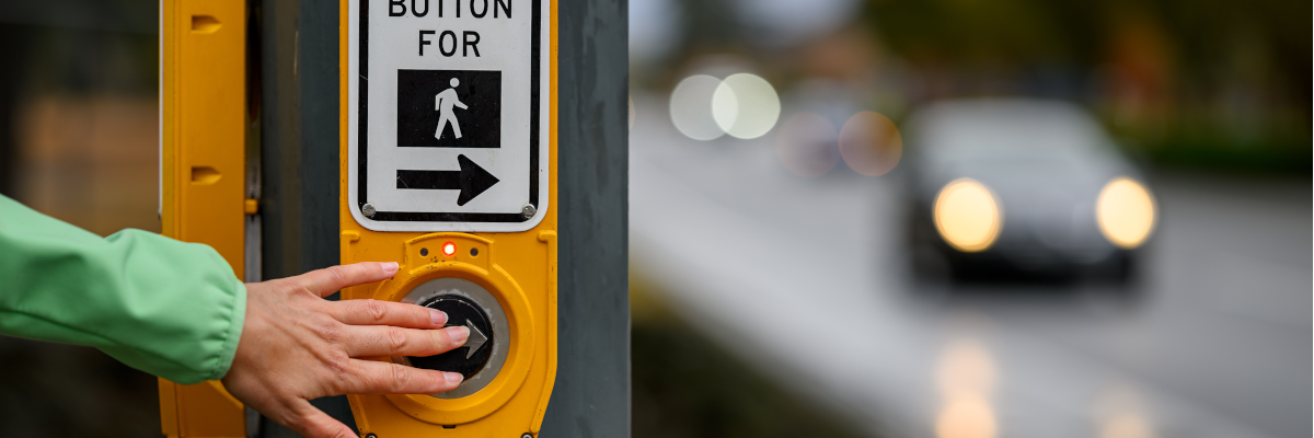 A hand pushes a pedestrian crosswalk button to cross an intersection.