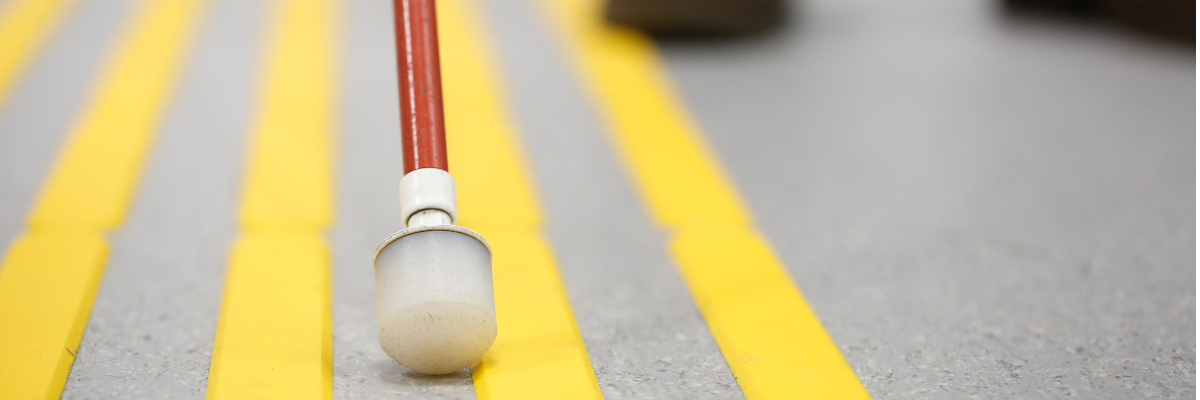 A white cane navigates a rubber wayfinding path on a sidewalk.