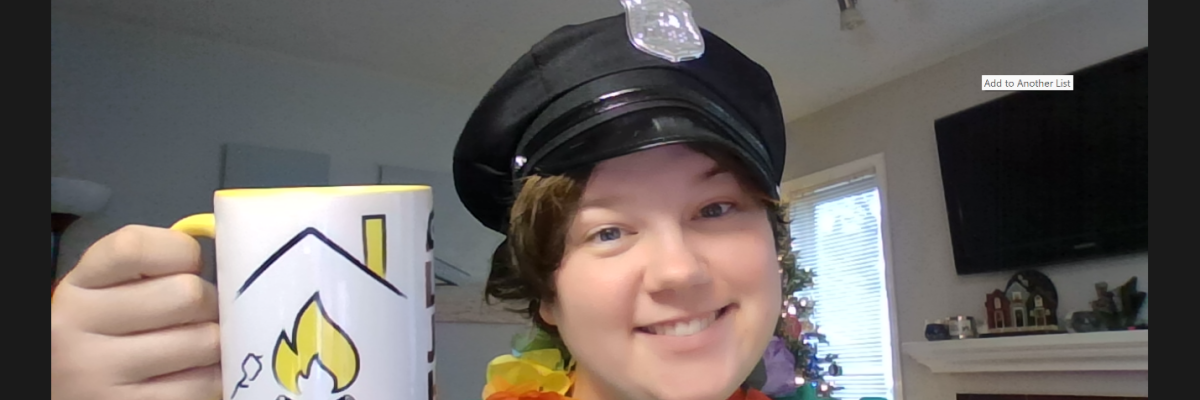 Sam is on a Zoom screen smiling. She is wearing a black police officer cap, a multi-colour Hawaiian lei, and is holding a CNIBLakeJoe@Home branded coffee mug.