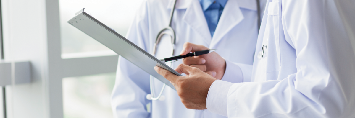 The two doctors wearing white lab coats. One doctor holds a clipboard – the other has a stethoscope around their neck.