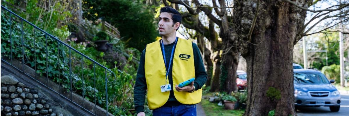 Collecteur de fonds d'INCA portant un gilet jaune, un badge d'identification et une tablette.