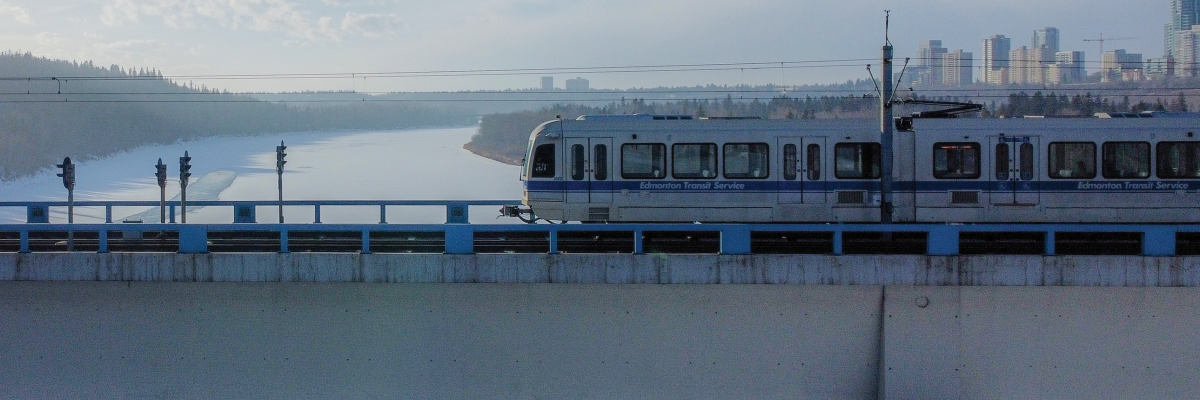 Un train léger d’Edmonton traverse un pont. Le pont s’élève au-dessus d’une étendue d'eau gelée, avec l’horizon d’Edmonton en arrière-plan. 