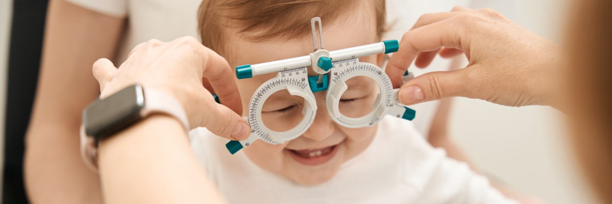 Un optométriste procède à un examen de la vue sur un jeune enfant. Il tient d'une main un cadre d'essai optométrique devant le visage de l'enfant.